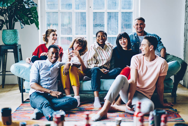 Happy multicultural people resting together at comfy home apartment sitting on cozy sofa, cheerful hipster guys laughing and relaxing in comfortable living room enjoying together leisure weekend - 写真・画像