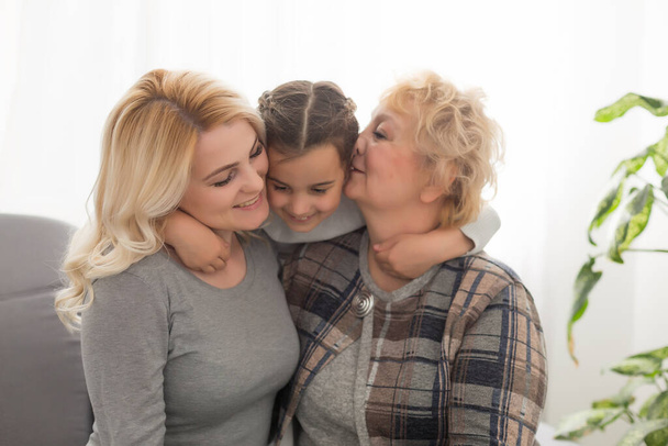 Retrato de tres generaciones de mujeres miran a la cámara posando para la imagen familiar, linda niña abrazo mamá y la abuela disfrutar del tiempo en casa, sonriente madre, hija y abuela pasar el fin de semana juntos - Foto, Imagen