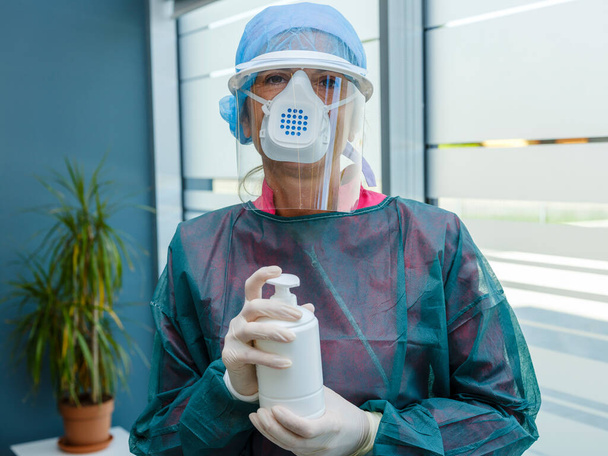 Vrouwelijke arts in medisch beschermend masker met een antibacteriële antiseptische gel voor desinfectie van de handen van bacteriën tijdens covid-19 virus epidemie en infectieziekten. Ontsmettingsmiddel, hygiëne en gezondheidszorg. - Foto, afbeelding