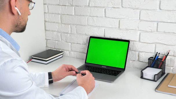 Doctor in hospital office looking green screen laptop listens talk patient - Photo, Image