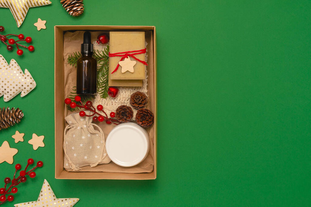 Present box with organic cosmetics on green background. Glass, wooden decorations. Zero waste Christmas concept. Flat lay top view, copy space - Фото, изображение