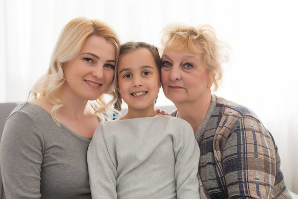 Portrait of three generations of women look at camera posing for family picture, cute little girl hug mom and granny enjoy time at home, smiling mother, daughter and grandmother spend weekend together - Photo, Image