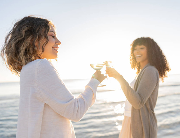 Glamour stijl foto van twee multiraciale modellen, blank en zwart Spaanse toast met een glas witte wijn aan het zeewater - zonsondergang of zonsopgang foto van twee vrouwen met de focus op blond haar - Foto, afbeelding