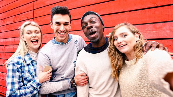 Glückliche multiethnische Freunde beim Gruppenselfie vor rotem Holzhintergrund - Millenials teilen lustige Geschichten in den sozialen Medien - Lifestyle- und Technologiekonzept auf warmem, lebendigem Filter - Foto, Bild