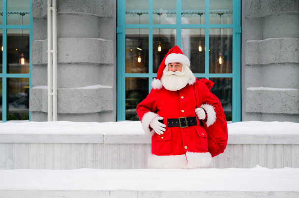 Pensive santa claus is leaning against the facade of a house in winter - Foto, Imagen