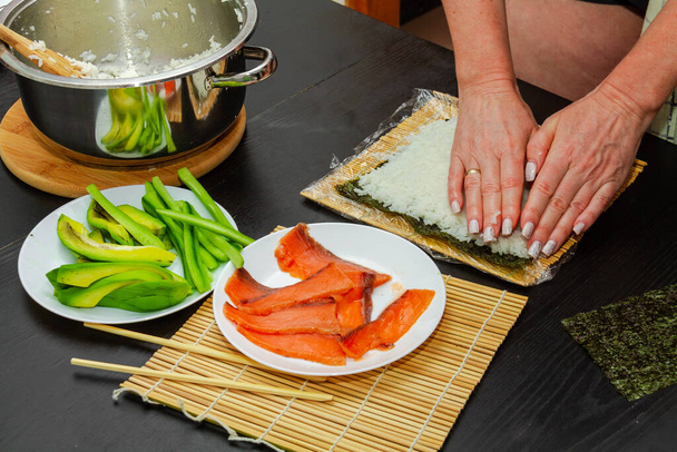 Der Herstellungsprozess von Sushi mit Gurken, Avocado und Lachs. - Foto, Bild
