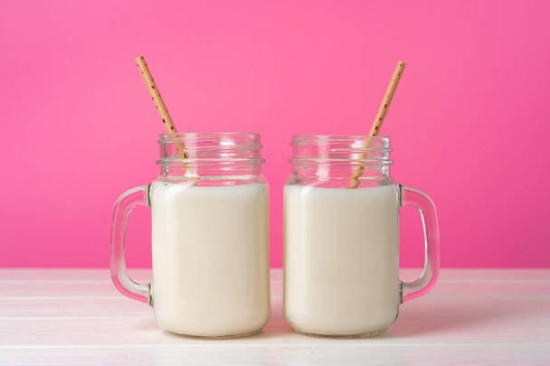 Glazen potten met gearomatiseerde milkshakes tegen een roze achtergrond - Foto, afbeelding