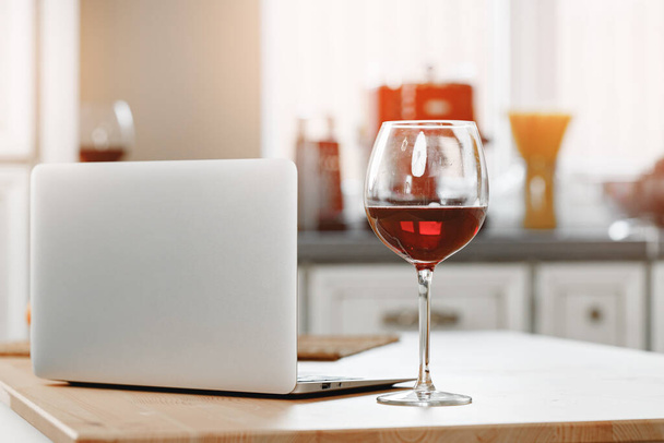 Laptop and glass of red wine on wooden kitchen table - Fotoğraf, Görsel