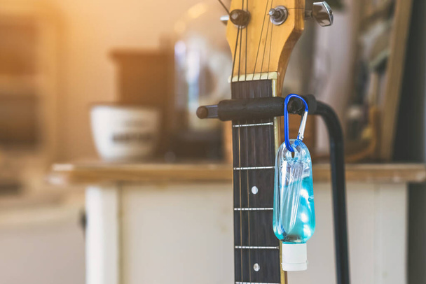 Mini gel alcolico portatile per prevenire il Coronavirus (Covid-19) per il paziente in quarantena prima di suonare la chitarra per rilassarsi appeso a un vecchio cavalletto della chitarra in una casa. Nuovo stile di vita normale - Foto, immagini