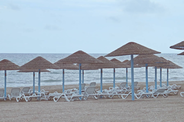Napágyak és szalma esernyők a romániai Olimp strandon. Üres strand egy felhős és hideg nyári napon. - Fotó, kép