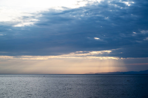 Égei-tenger naplementekor, napfény áttör a felhők között, terep látható a távolban, Görögország - Fotó, kép
