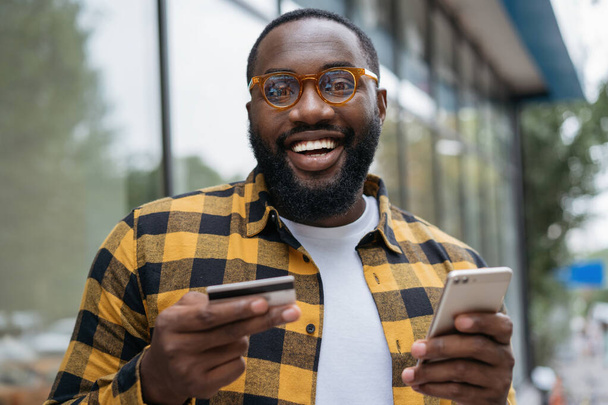 Elinde kredi kartı olan, internetten alışveriş yapan gülümseyen Afrikalı Amerikalı bir adamın portresi. - Fotoğraf, Görsel