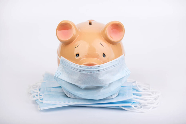 Covid 19 concept. Piggy bank with pile of medical face masks isolated background.health concept  - 写真・画像