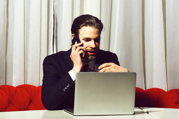 bearded man, businessman holding glass of whiskey works at laptop - Photo, image