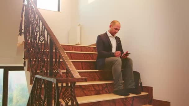 Biznesmen piszący na smartfonie siedzącym na schodach - Materiał filmowy, wideo