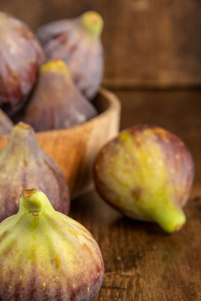 Top view of figs, with more background in wooden bowl, with selective focus, on wooden background, in vertical - Foto, Imagen