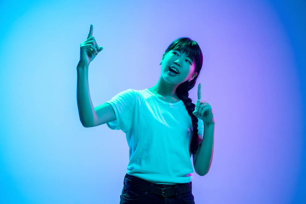 Young asian womans portrait on gradient blue-purple studio background in neon light - Photo, image
