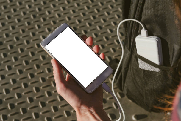 Mock up of a smartphone in a man's hand. Charging from a power bank in a backpack pocket - Φωτογραφία, εικόνα