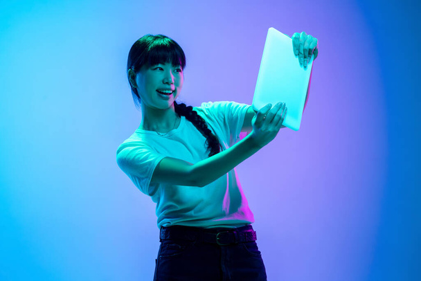 Young asian womans portrait on gradient blue-purple studio background in neon light - Photo, Image