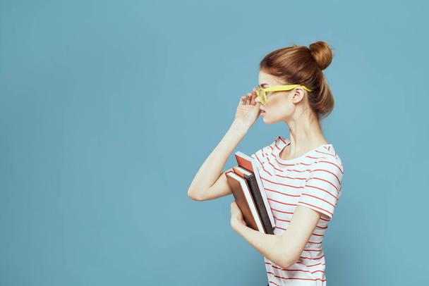 Γυναίκα φοιτητής με βιβλία στα χέρια σε μπλε φόντο και κίτρινα γυαλιά μοντέλο hairstyle περικοπή άποψη - Φωτογραφία, εικόνα