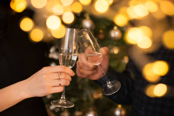 man en vrouw clink glazen champagne tegen de achtergrond van een kerstboom - Foto, afbeelding
