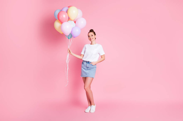 Full body photo of attractive pretty lady pretty bun summer vacation good mood hold many air balloons birthday celebration wear white t-shirt mini skirt shoes isolated pink color background - 写真・画像