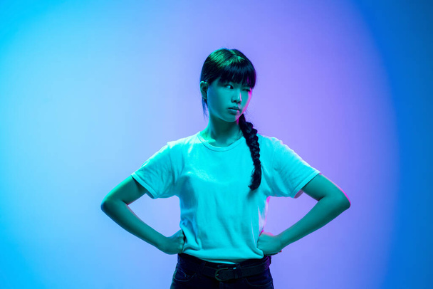 Young asian womans portrait on gradient blue-purple studio background in neon light - Foto, imagen