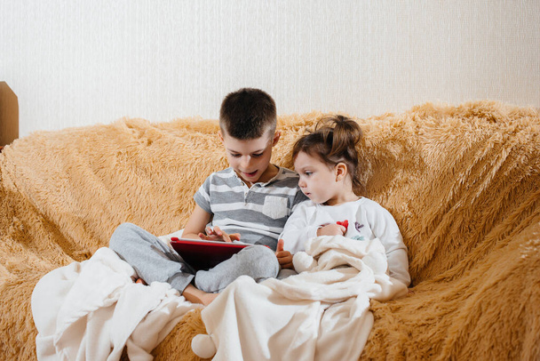 Brother and sister play on the couch in the tablet - Φωτογραφία, εικόνα