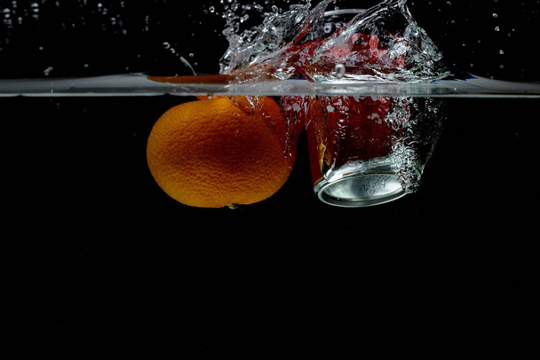 Прекрасний вид на мандарин і содову банку, що падає у воду і плаває на поверхні. Прекрасні фони. Концепція їжі та напоїв
. - Фото, зображення