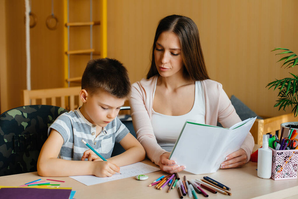 A young mother is doing homework with her son at home. Parents and training - Valokuva, kuva