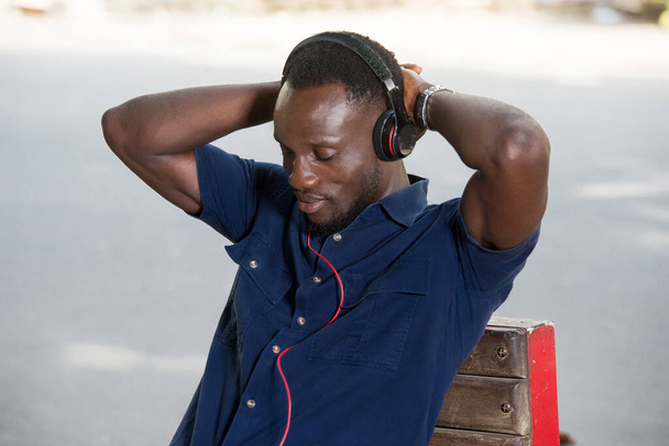 joven sentado al aire libre escuchando música usando auriculares. - Foto, imagen