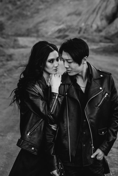 An Asian couple in love in black leather clothes walk in nature among the trees. Black-white - Φωτογραφία, εικόνα