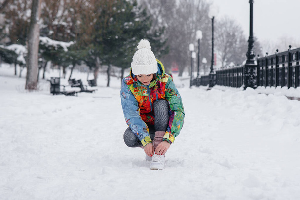 A young athletic girl ties her shoes on a frosty and snowy day. Fitness, running - Photo, Image