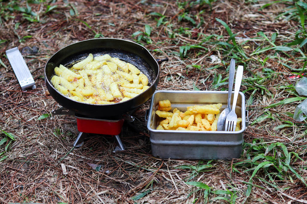 the process of frying potatoes outdoors with a red mini gas stove and black frying pan - Photo, Image