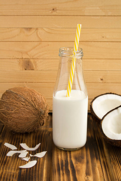 Kokosmelk in de glazen fles en kokosnoten op de houten ondergrond - Foto, afbeelding