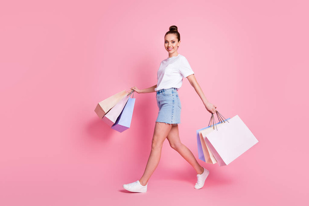 Full size profile side photo of positive cheerful girl go walk trip have shopping day hold many bags wear white t-shirt sneakers isolated over pastel color background - Foto, Imagem