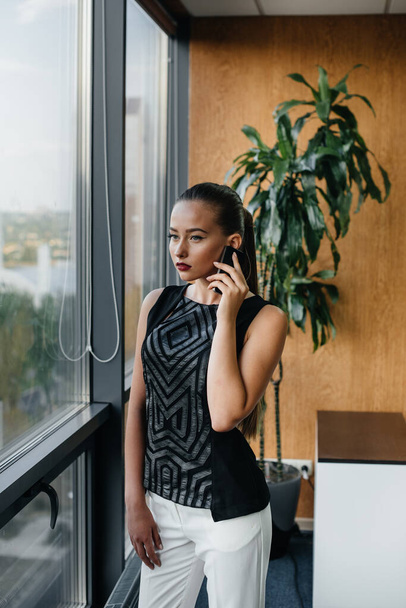 The secretary is talking on the phone near the window in the office - Fotografie, Obrázek