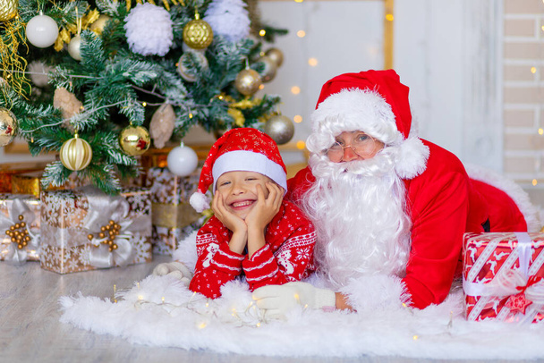 Санта-Клаус с ребенком рядом с рождественской елкой обнимает - Фото, изображение