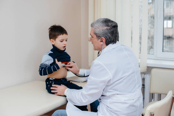 A young boy is listened to and treated by an experienced doctor in a modern clinic. A virus, and an epidemic - Fotografie, Obrázek