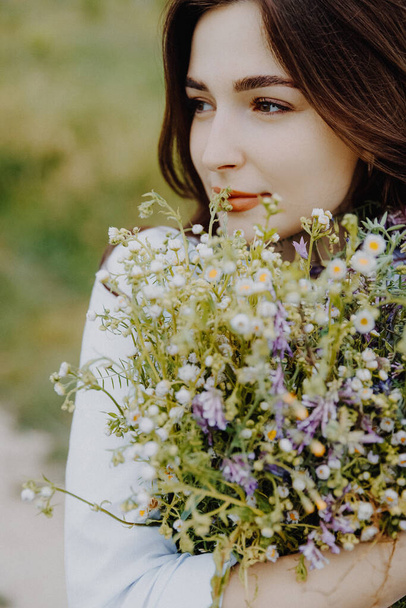 attractive woman dressed in a long shirt posing for a photo in a field among weeds and wildflowers - Foto, afbeelding