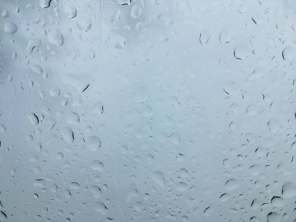 Gotas de agua en la superficie del vidrio. Ventana húmeda después de la lluvia. Fondo abstracto en tonos grises - Foto, Imagen