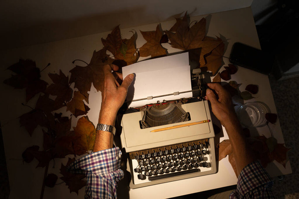 Vista superior de las manos del hombre en una máquina de escribir con hojas de otoño, escritor inspirado - Foto, imagen