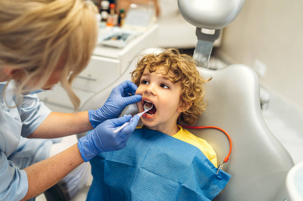 Cute young boy visiting dentist, having his teeth checked by female dentist in dental office - Foto, Imagen