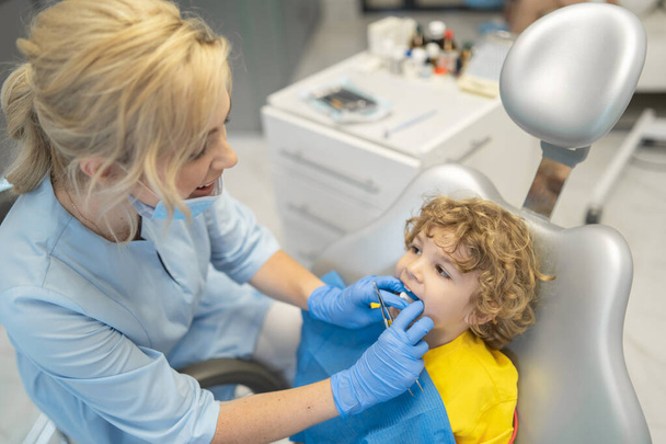 Cute young boy visiting dentist, having his teeth checked by female dentist in dental office - Foto, Imagem