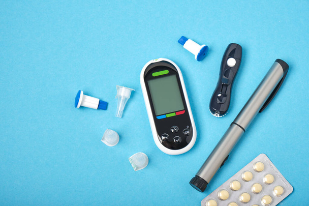 糖尿病の血糖値計モニター、スペア針付きのランネット、インスリンと錠剤を注入するための注射器ペン、注射用の新しい滅菌針、青の背景、コピー場所のトップビュー - 写真・画像
