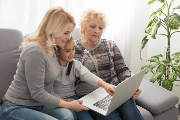 Felice tre generazioni di donne si siedono rilassarsi sul divano ridere guardando video divertente sul computer portatile, sorridendo donne positive nonna, madre e figlia si divertono a riposare sul divano godersi il film sul computer - Foto, immagini