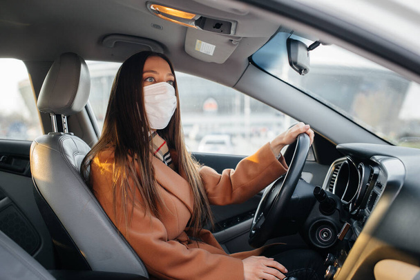 A young girl sits behind the wheel in the car in the mask during the global pandemic and coronavirus. Quarantine - Foto, Bild