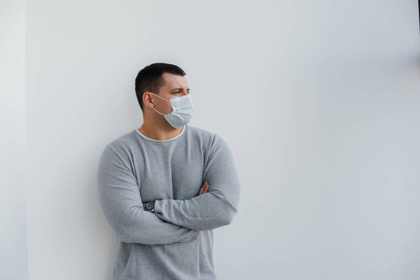 A young man stands on a gray background wearing a mask during a quarantine with free space. Quarantine in the mask - Valokuva, kuva