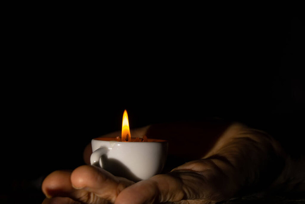 κερί φλόγα σε κύπελλα στα χέρια μιας ηλικιωμένης γυναίκας στο σκοτάδι, κερί φως - Φωτογραφία, εικόνα