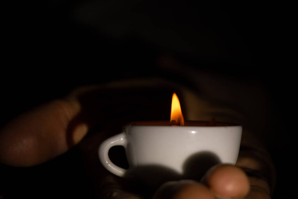 fiamma di candela in tazze sulle mani di una vecchia donna al buio, luce di candela - Foto, immagini